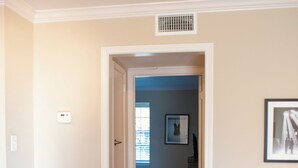 A hallway with a glass table, a framed picture on the wall, and a vent on the ceiling.