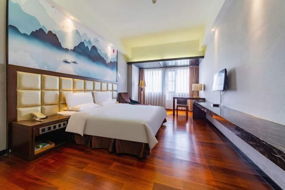 A hotel room with a large bed, a desk, a chair, a TV, and a painting on the wall.