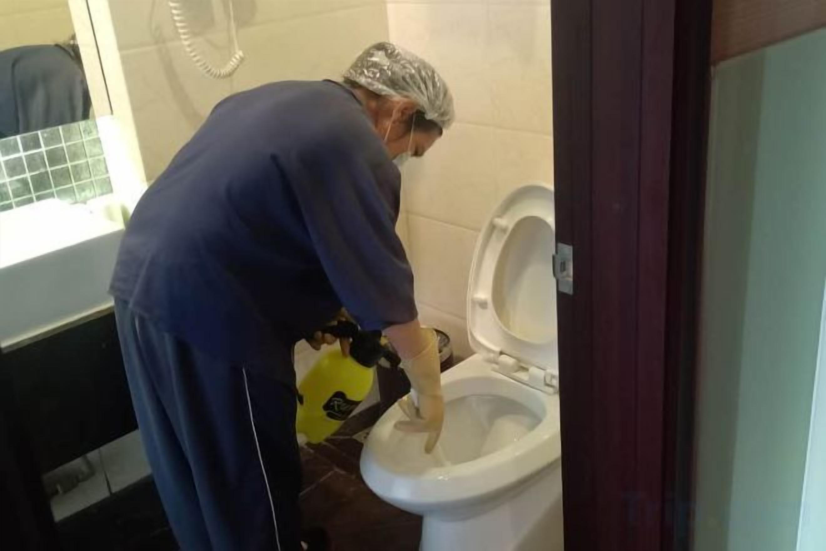 A person cleaning a toilet in a bathroom.
