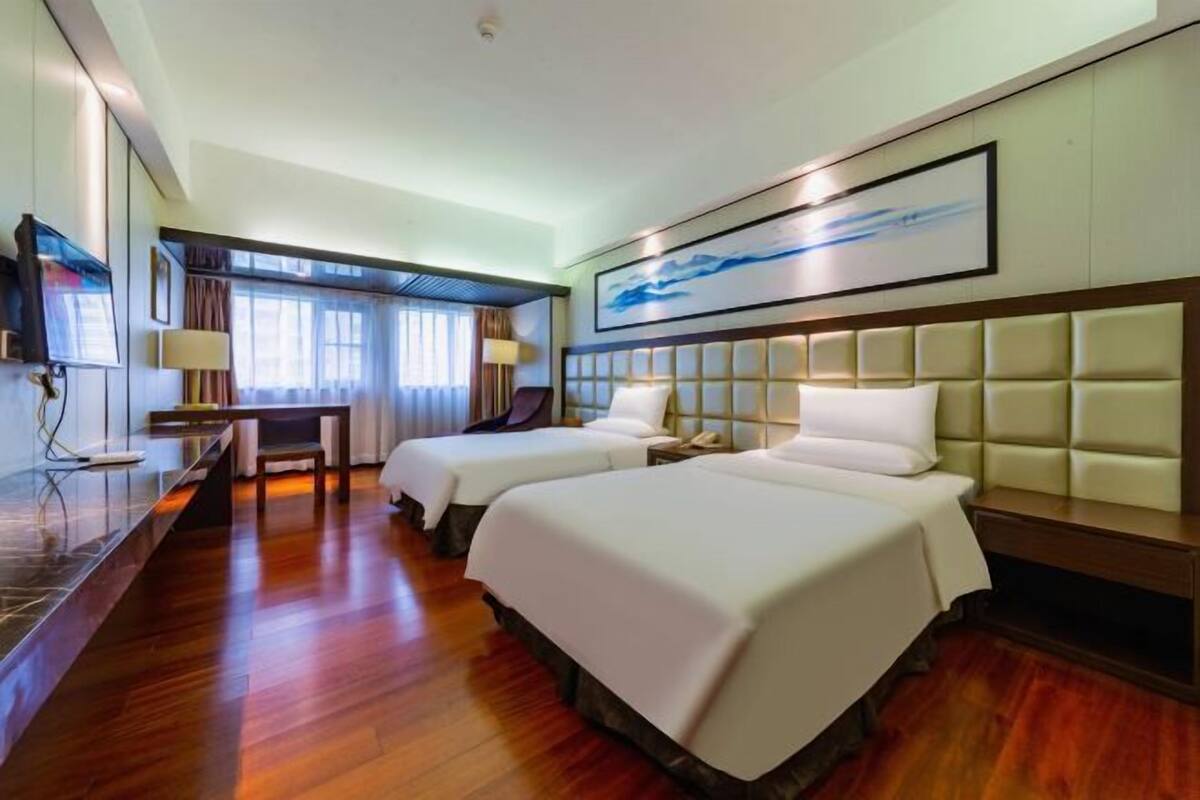 A hotel room with two beds, a desk, and a television.
