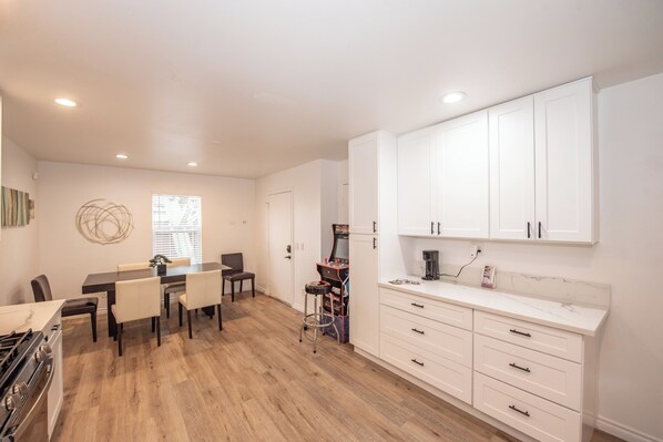 A modern kitchen with white cabinets, a dining area with a table and chairs, and a small bar area with stools.
