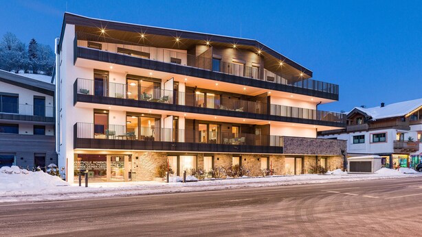 A multi-story hotel with balconies, a stone facade, and a snow-covered ground. - Apartment fuer 2 Personen (Brixen im Thale)