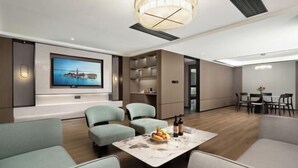 A modern living room with a flat-screen TV, comfortable seating, a coffee table with fruit, and a dining area with chairs.