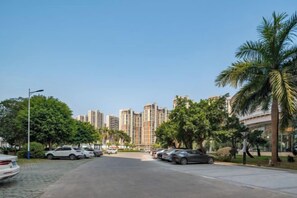 A residential street with parked cars, palm trees, and high-rise buildings in the background. - Jinxin Huayuan Hotel (Shantou)