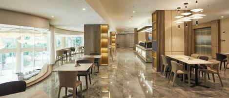 Un comedor de hotel moderno con suelo de mármol, varias mesas y vistas al exterior.