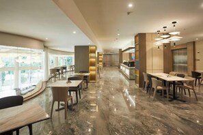 Un comedor de hotel moderno con suelo de mármol, varias mesas y vistas al exterior.