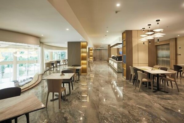 Un comedor de hotel moderno con suelo de mármol, varias mesas y vistas al exterior.