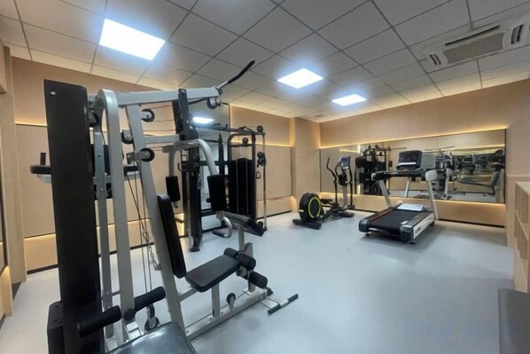 A gym with various exercise equipment, including a bench press, a squat rack, and a treadmill. - Jinxin Huayuan Hotel (Shantou)