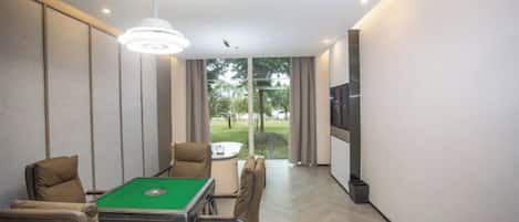 A room with a pool table, comfortable seating, a television, and a view of the outdoors.