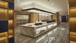 A modern hotel lobby with a marble reception desk, wooden paneling, and a glass elevator.