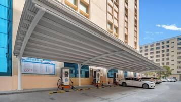 A covered outdoor area with fuel pumps, a car, and a building with multiple windows.