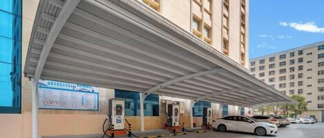 A covered outdoor area with fuel pumps, a car, and a building with multiple windows.