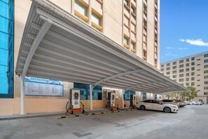 Un área al aire libre techada con surtidores de combustible, un coche y un edificio con varias ventanas.