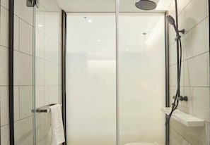 Cabina de ducha con paredes de vidrio, una ducha de mano, un perchero y un estante pequeño.
