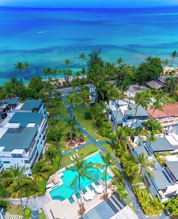 An aerial view of a resort with a swimming pool surrounded by palm trees and a view of the ocean.
