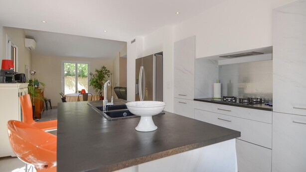 A modern kitchen with white cabinets, a black countertop, and a white bowl. There is a dining area with orange chairs and a table. - Cozy home in Marguerittes (Marguerittes)