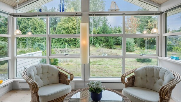 A conservatory with large windows, wicker chairs, and a glass table with a vase.