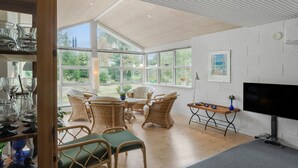 A spacious room with large windows, wicker furniture, and a flat-screen TV.