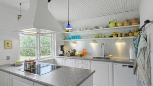 A modern kitchen with white cabinetry, a granite countertop, a built-in stove, and a window providing a view of greenery outside.