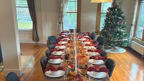 A dining room with a long table set for a meal, surrounded by chairs, a Christmas tree, and large windows. - HollyKissHudsonValley Renovated 1900 Lodge, Full House. (Catskill)