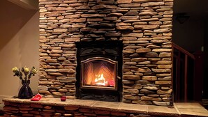 A stone fireplace with a fire, a vase with flowers, and a red candle on a wooden mantel. - HollyKissHudsonValley Renovated 1900 Lodge, Full House. (Catskill)