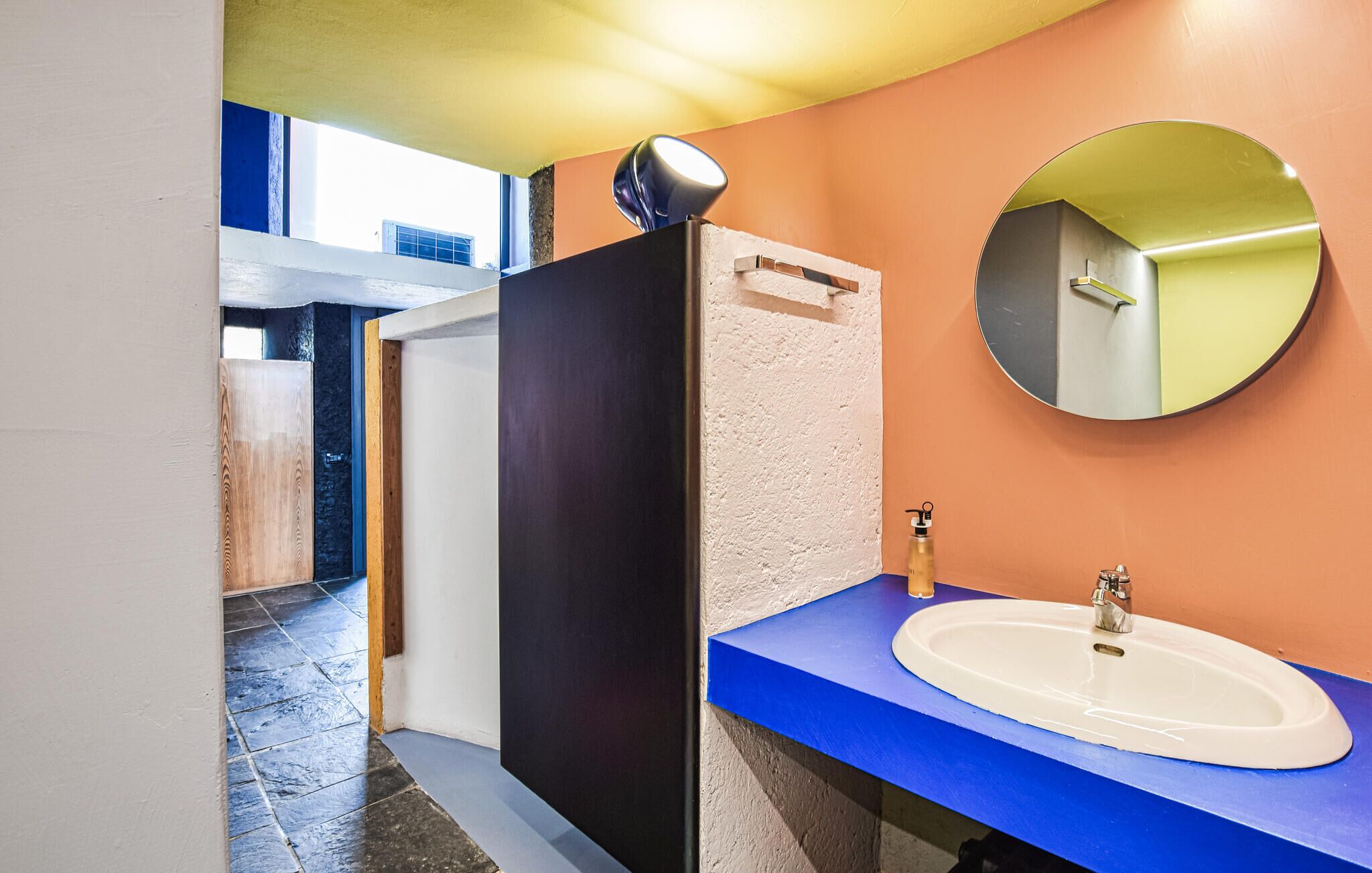 A bathroom with a blue countertop, a white sink, a round mirror, and a shower area.