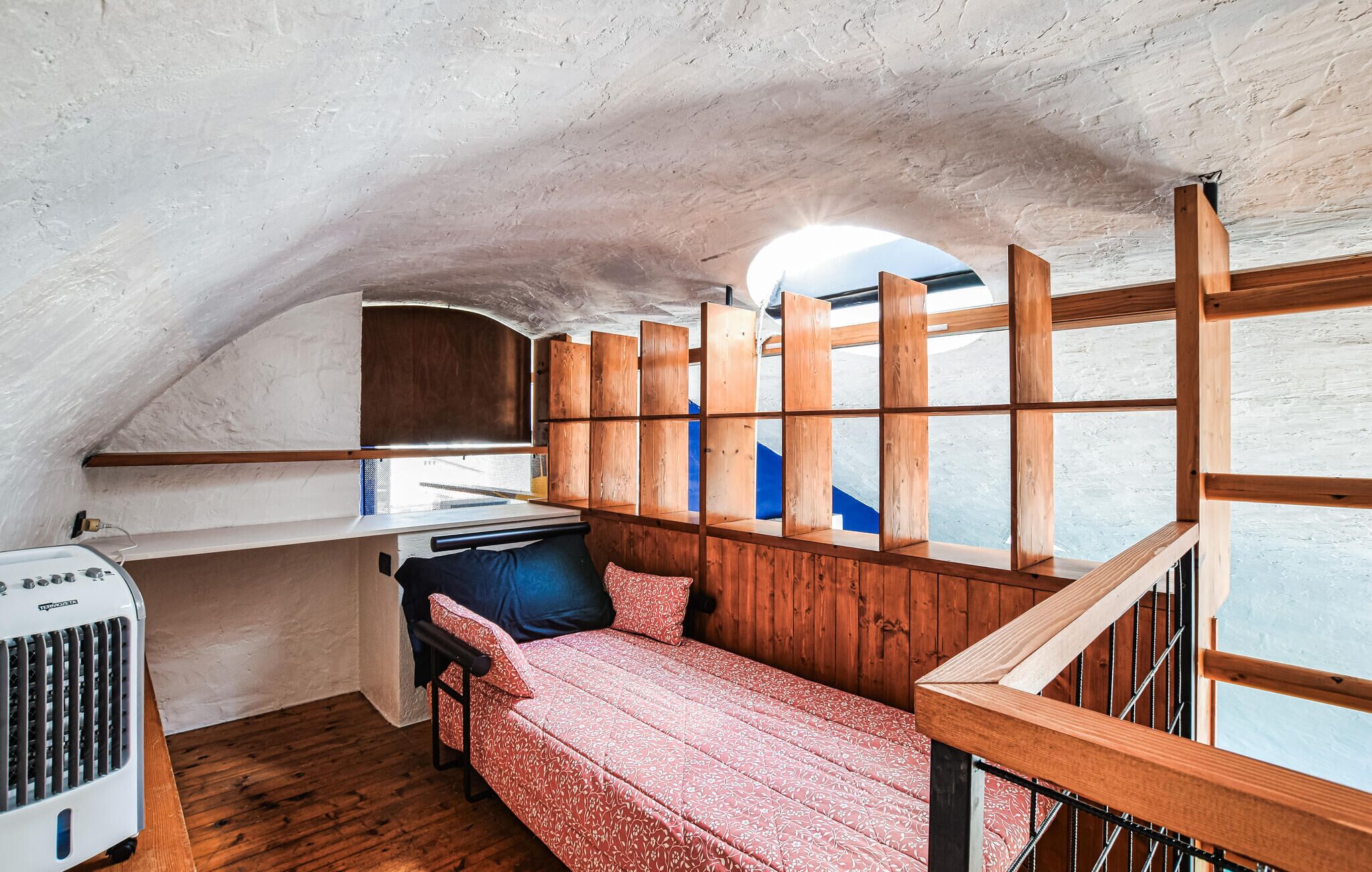 Une pièce compacte, aménagée dans un style mansardé, avec un lit superposé, une petite kitchenette et une cloison en bois.