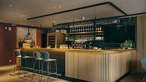 A modern bar area with a wooden counter, bar stools, and shelves stocked with bottles and glasses. - Amazing apartment in Brixen im Thale (Brixen im Thale)