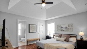 Une chambre à coucher avec un lit, des tables de chevet, un ventilateur de plafond et des œuvres d’art accrochées aux murs.