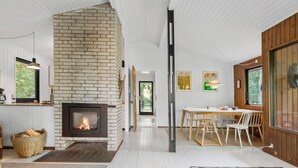 Een modern interieur met een metselwerk open haard, witte houten wanden en een eethoek met een houten tafel en stoelen.