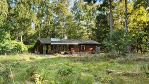 Een rustieke houten hut met een overdekte veranda, omringd door dicht bos.