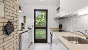 Een moderne keuken met witte kasten, een zwarte deur naar een tuin en een hanglamp.
