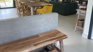 Un soggiorno moderno con una panca in legno, un tavolo da pranzo e sedie. Una grande finestra offre luce naturale e vista sul verde.