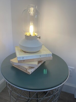 Ett bord med en lampa med glasskärm och staplar av böcker på.