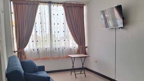 Une pièce avec un canapé bleu, une petite table et un téléviseur fixé au mur.