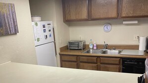 Una cucina con mobili in legno, un piano di lavoro bianco, un frigorifero, un tostapane, un lavello e una sveglia appesa al muro.