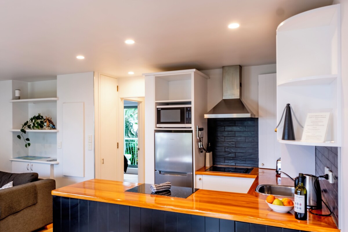 A modern kitchen with a built-in microwave, a stainless steel refrigerator, and a black brick backsplash.
