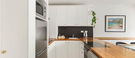 A modern kitchen with white cabinets, a wooden countertop, and a stainless steel range hood.