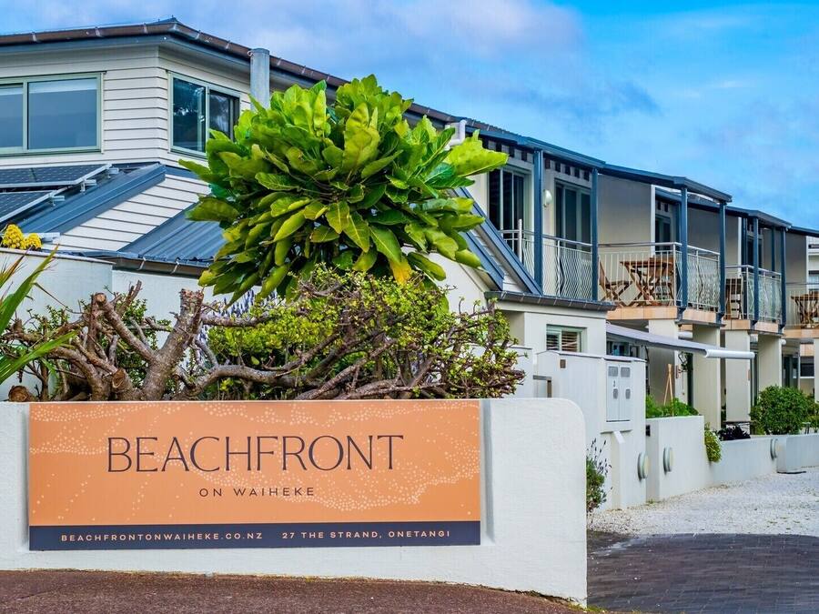 Une propriété située en bord de mer, avec une pancarte indiquant « EN BORD DE MER À WAIHEKE », et un bâtiment moderne doté de balcons.