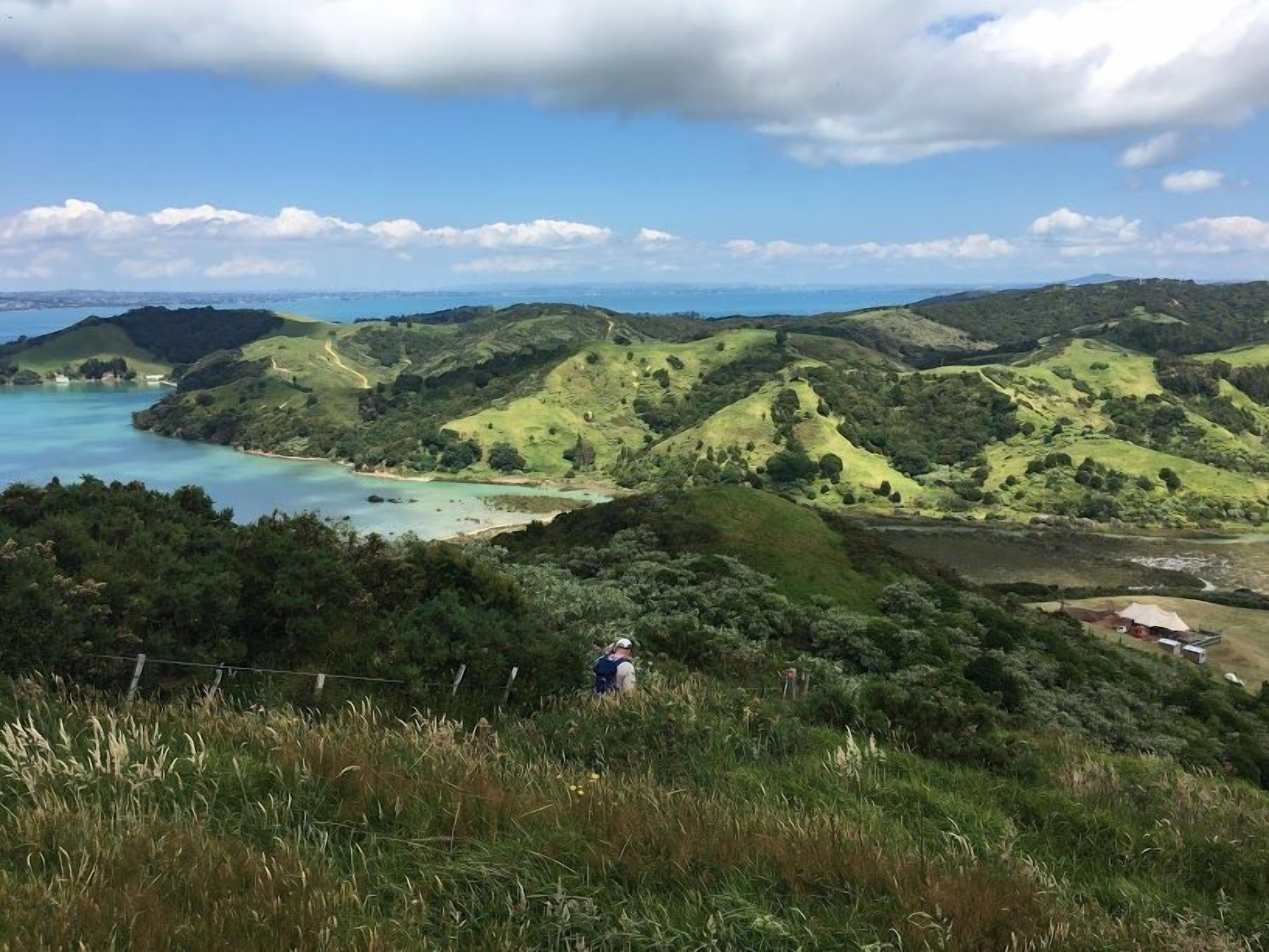 A hilly landscape with a coastal view, a person hiking, and a small structure in the distance.