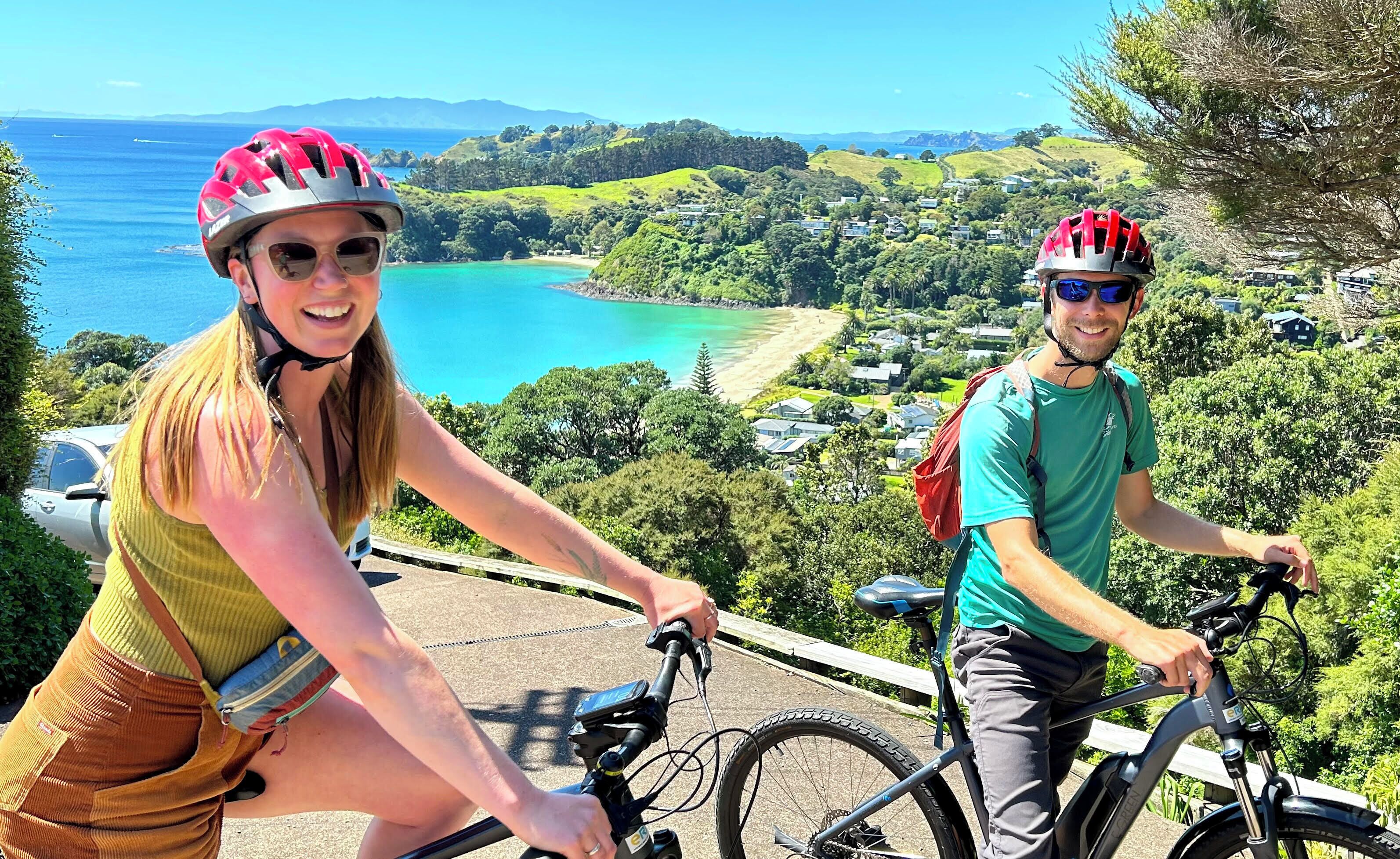 Two people on bicycles overlooking a coastal landscape with houses and greenery.