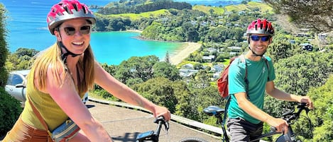 Dos personas en bicicleta contemplando un paisaje costero con casas y vegetación.