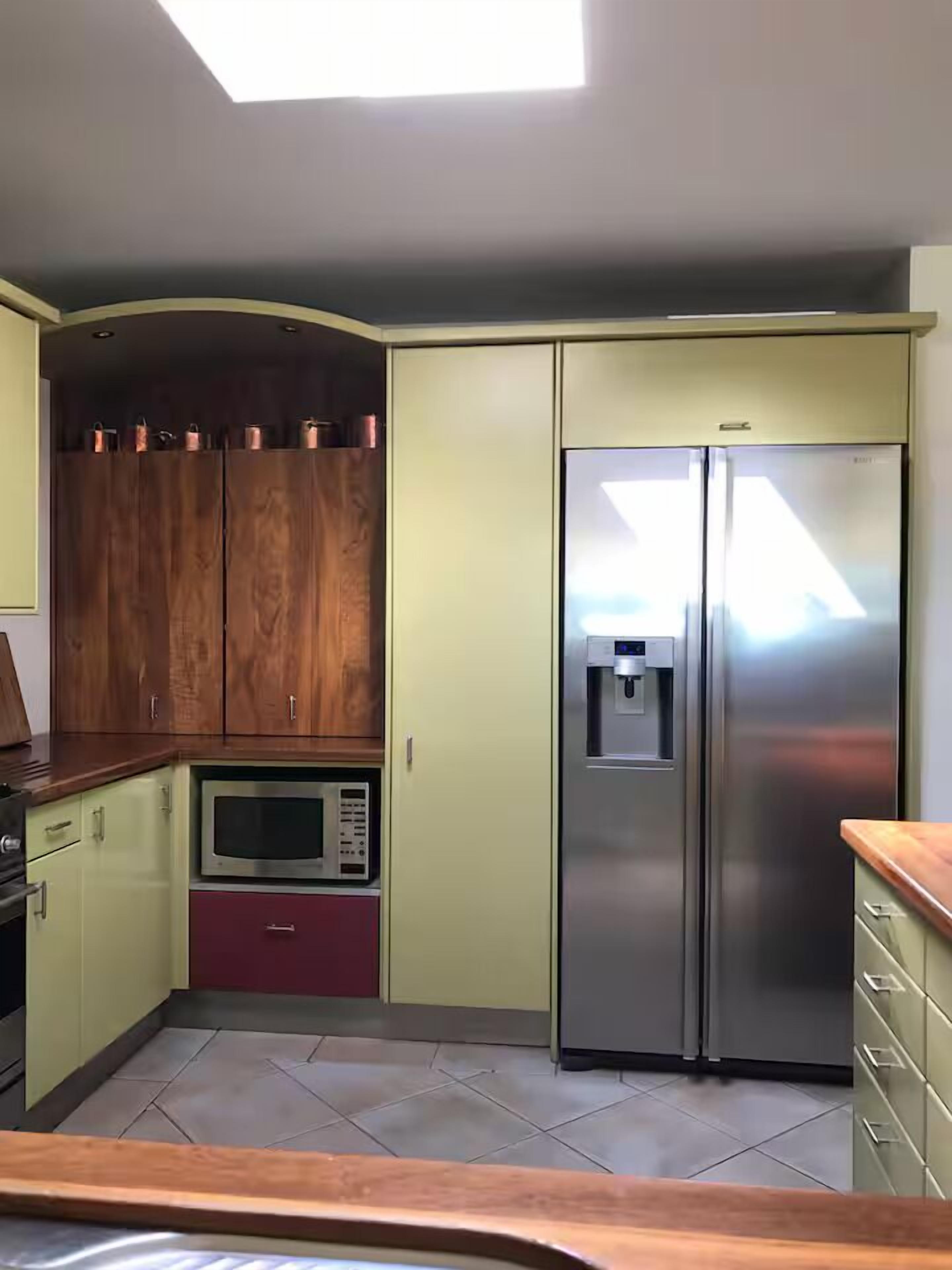 A compact kitchen with a built-in microwave, a stainless steel refrigerator, and wooden cabinets.