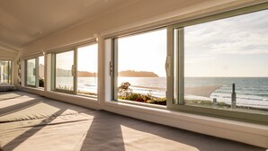 Ein Zimmer mit großen Fenstern, die Blick auf einen Strand bieten, ein Bett mit Meerblick und eine Aussicht auf den Ozean sowie ein entferntes Land.