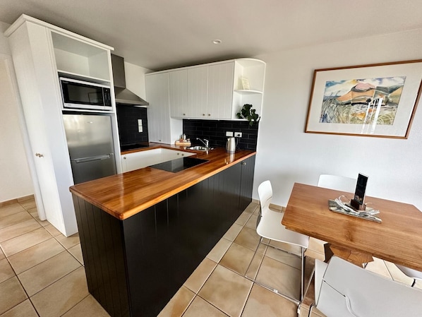 A modern kitchen with white cabinets, a black countertop, and a stainless steel refrigerator. - Beachfront on Waiheke (Waiheke Island)