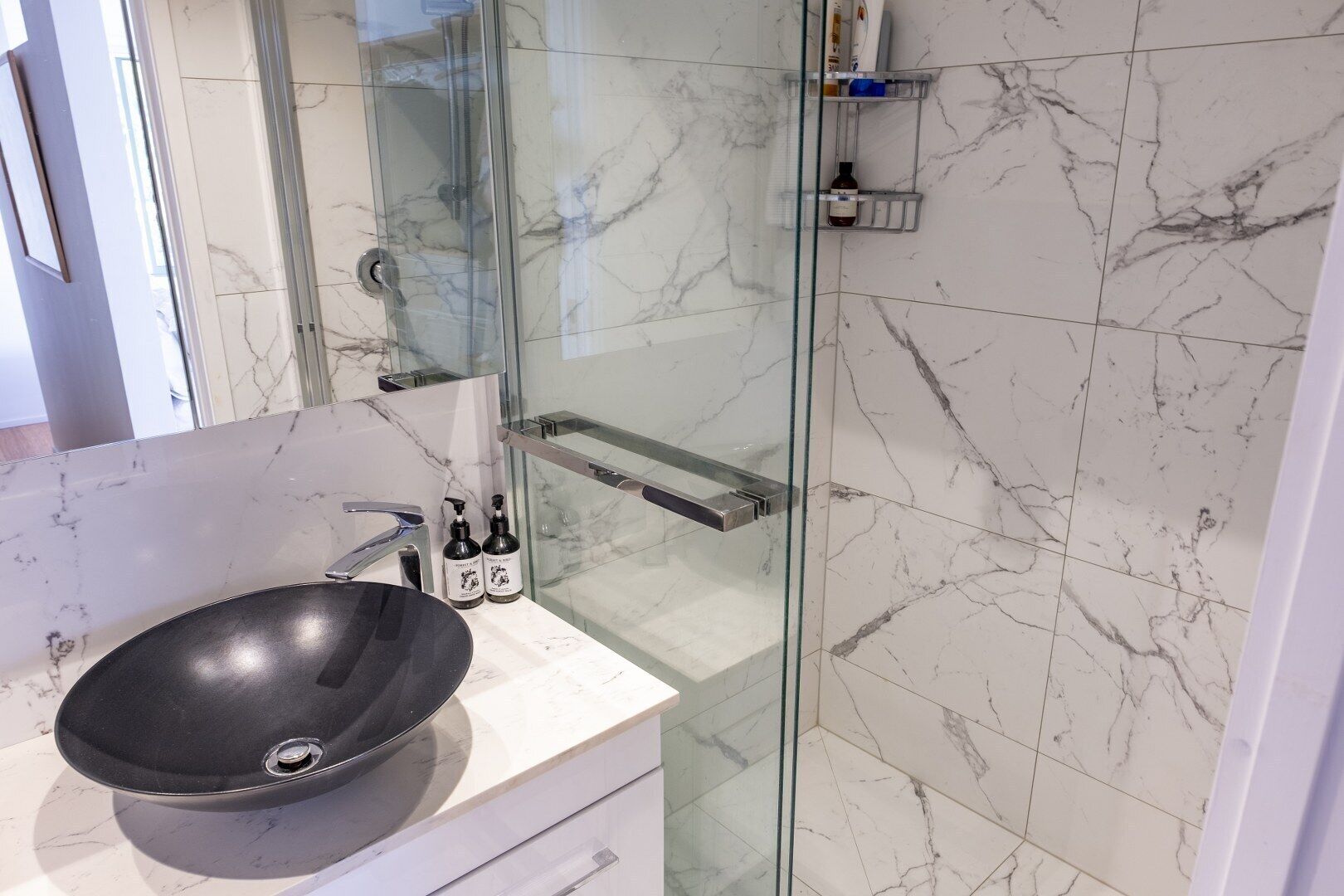 A modern bathroom with a glass shower enclosure, a black sink, and marble tiles.