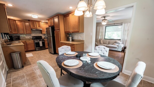 A modern kitchen with wooden cabinets, stainless steel appliances, and a dining area with a round table and chairs. - Modern Stay on Green Valley - 2.5 mi to downtown Greensboro (Greensboro)