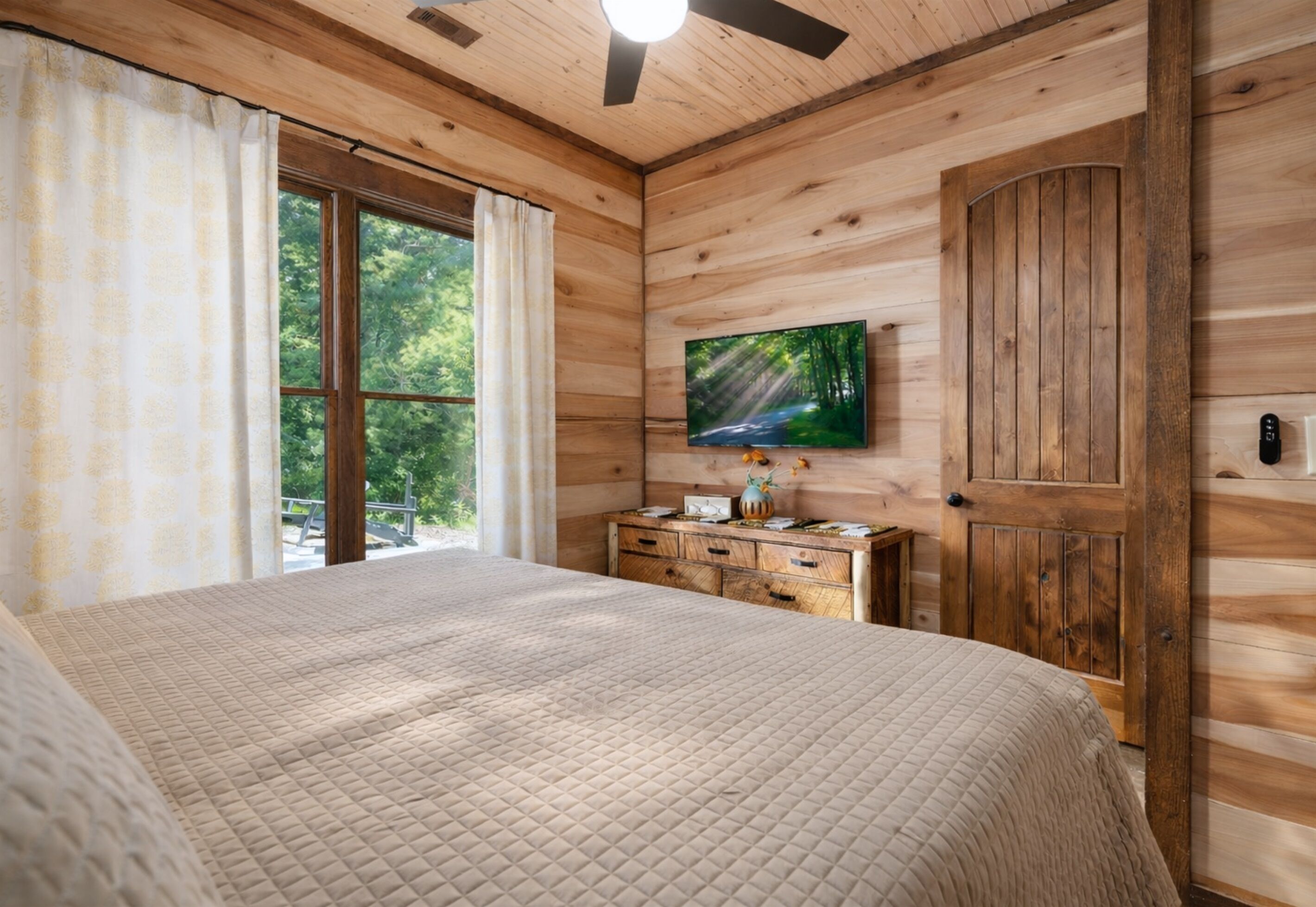 A wooden cabin bedroom with a bed, dresser, and a TV mounted on the wall.
