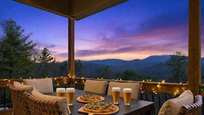 Une terrasse en bois avec une table dressée pour deux personnes, deux pizzas et quatre bières.