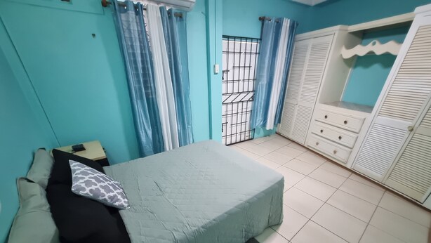 Un dormitorio con cama, mesita de noche, armario y ventana con cortinas.